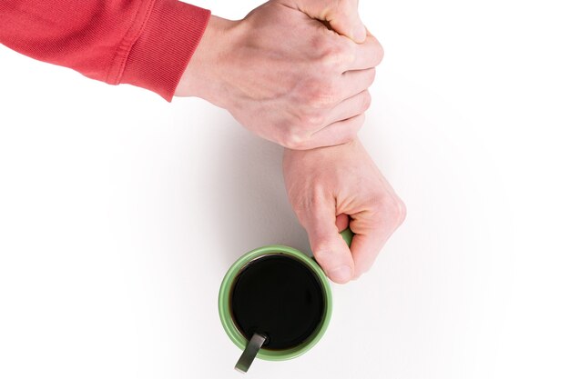 One hand holds a green cup of coffee other hand grabbed that arm to stop drinking hot beverage.