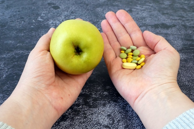 Una mano con mele verdi e l'altra mano con pillole, primo piano