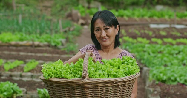 Photo one happy asian american woman standing in green field with local farm in background portrait of a smiling local small business owner showing food produce