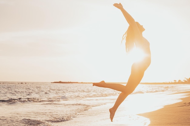 One happy and healthy young woman jumping on the sand of the beach having fun and enjoying summer outdoors Beautiful attractive girl playing