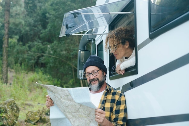 幸せな旅行者のカップルが紙のガイドマップを一緒に見て、次の旅行先の計画を立てます。バンに住んでいます。遊牧民、バンライフ。代替車両での休暇旅行。ロードトリップの計画