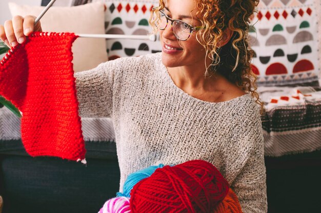 Una donna felice a casa sembra soddisfatta un lavoro a maglia con lana rossa donna a casa con hobby che fa vestiti caldi la signora dei giovani felici sorridono e si godono il tempo libero al coperto lavoro di concetto di abbigliamento fatto a mano