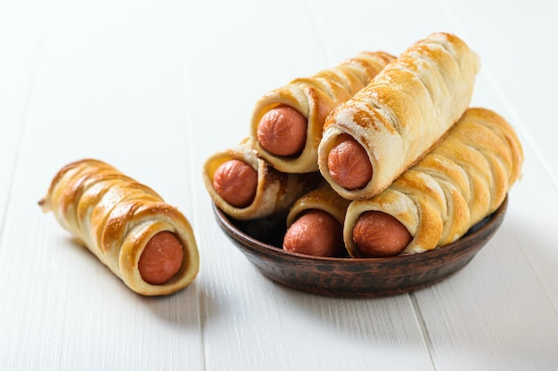 One homemade sausage in a batter on the table and five sausages in a clay bowl on a white rustic table