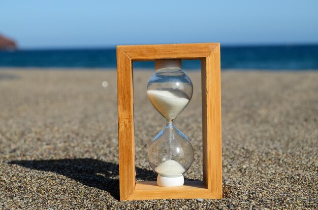 Foto una clessidra sulla spiaggia di sabbia vicino al concetto di tempo dell'oceano