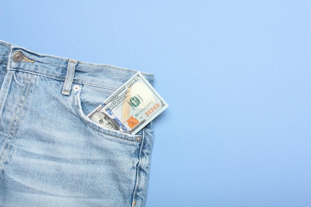 One hundred dollar bill in jeans pocket on blue background