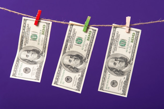 One hundred dollars hanging on clothesline with wooden clips on blue background