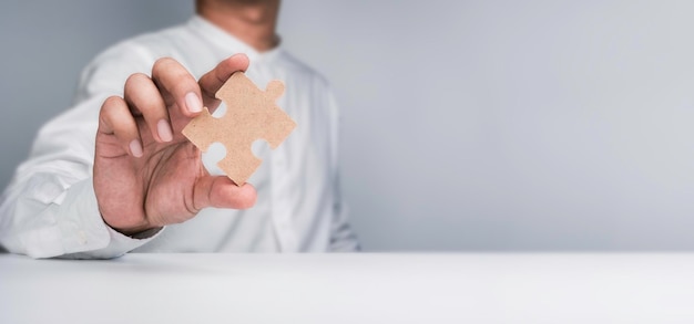 A one jigsaw puzzle element in a businessman's hand Person hand showing a piece of the important jigsaw puzzle on the table and white background with copy space Business solution and idea concept