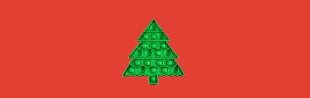 Photo one kids anti stress pop it toy in form of green christmas tree on red banner copy space