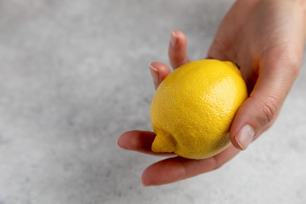 One lemon in hand and over grey background