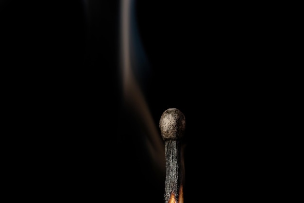 One lonely burnt match with some slight smoke against black background. Concept of loneliness