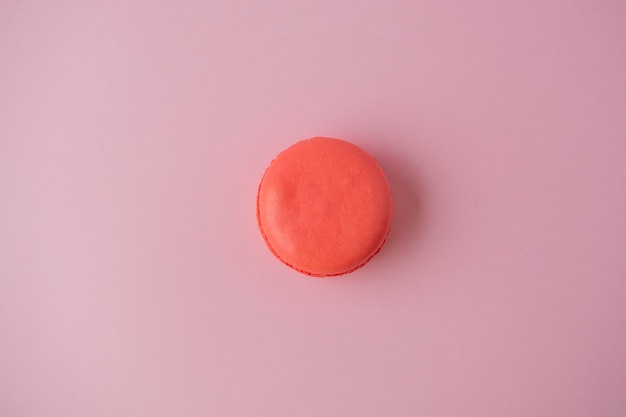 One macaroon cookie is orange on a pink paper background. Minimalism, delicious dessert