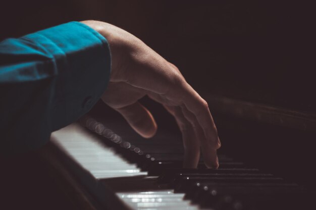 One male hand on the piano The palm lies on the keys and plays the keyboard instrument in the music school student learns to play hands pianist black dark background