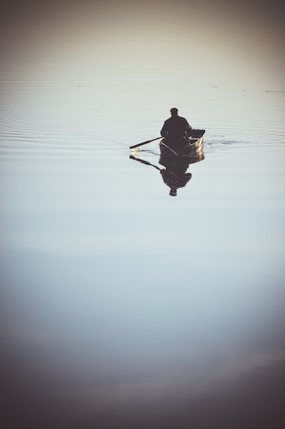 Un uomo in una piccola barca a vela in barca a remi sul fiume lago. fiume con una superficie liscia a specchio dell'acqua. tempo tranquillo, calmo, senza vento