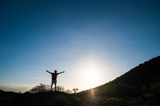 太陽を見ながら両手を広げて丘の中腹でセッションを実行した後の日没の一人の男-フィットネスと健康的なライフスタイルとコンセプト
