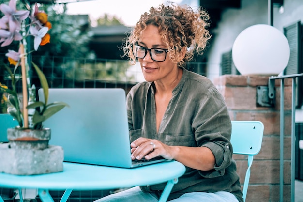 One modern happy serene woman using computer outdoor at home in garden Pretty female writing on laptop outside house Alternative workplace and wireless connection technology People with notebook