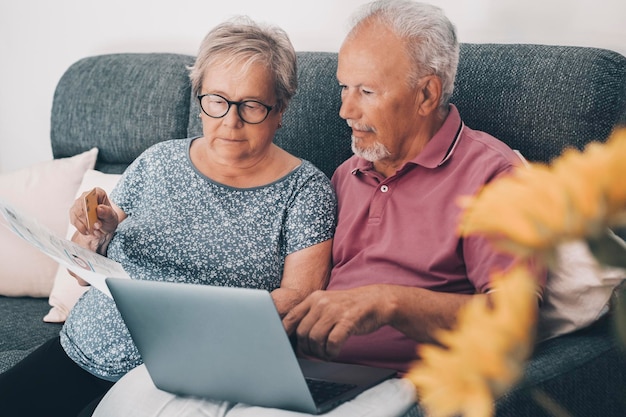 집에 있는 한 노인 부부는 웹 뱅킹 앱으로 온라인으로 청구서를 지불하고 문서의 금액을 확인합니다 노인 및 현대 기술 실생활 컴퓨터와 인터넷을 사용하는 성숙한 남녀
