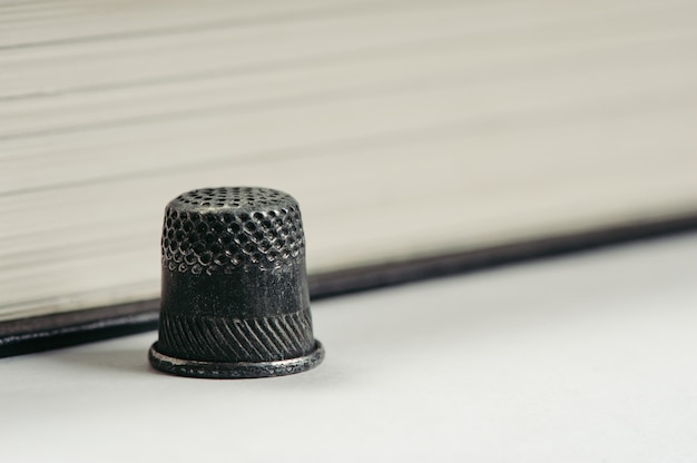 One old thimble against the background of the pages of the book. Monochrome.