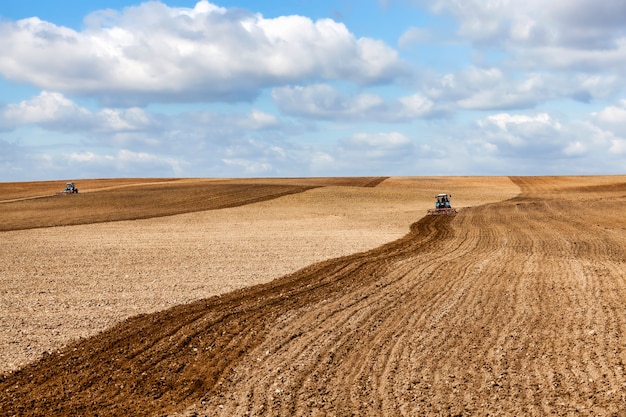 한 낡은 트랙터가 밭에서 흙을 갈아서 파종을 위해 밭을 준비하고, 흐린 날의 풍경