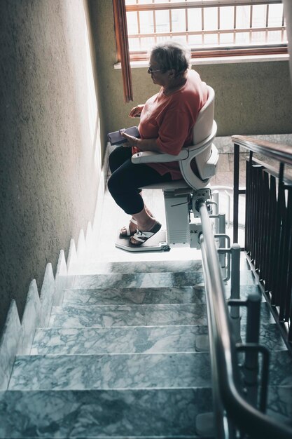 One old woman with legs problems use electric engine chair to up the stairs at home in a building Tecnology to help elderly life for people concept