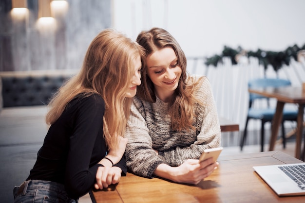 One-on-one meeting. Twee jonge zakelijke vrouwen zitten aan tafel in café. Girl toont haar vriend afbeelding op het scherm van de smartphone. Op tafel is gesloten notebook. Vrienden ontmoeten