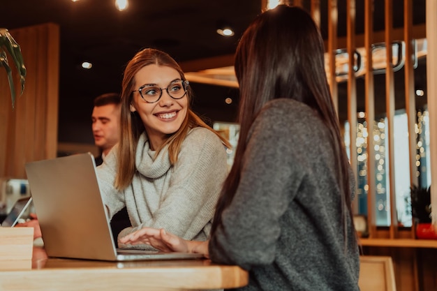 One-on-one meeting.Two young business women sitting at table in cafe. Girl shows colleague information on laptop screen. Girl using smartphone, blogging. Teamwork, business meeting. Freelancers workin