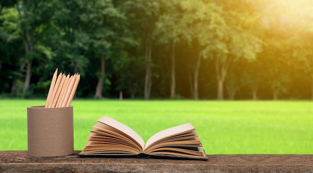 One open old book and a pencil case on a wooden table beautiful green lawn and forest background