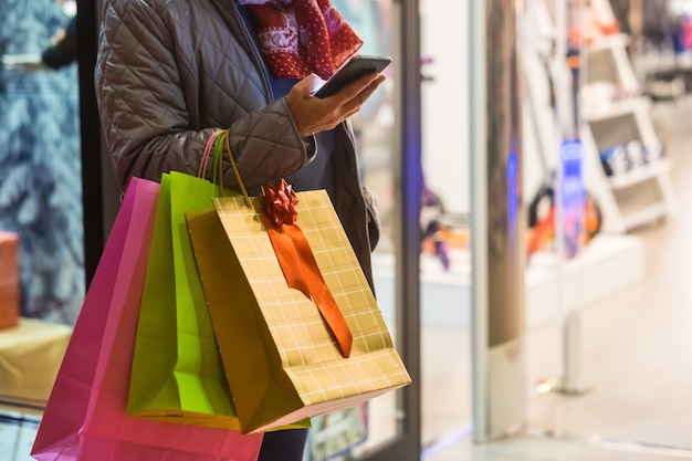 One people alone. a senior woman enjoys evening shopping while
taking advantage of offers and discounts. on his arm a lot of
shopping bags while she looks at her cell phone