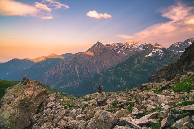 One person sitting on rocky terrain and watching a colorful sunrise high up in the Alps. 