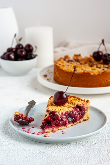 One piece of summer cherry pie in a plate with whole pie on the background