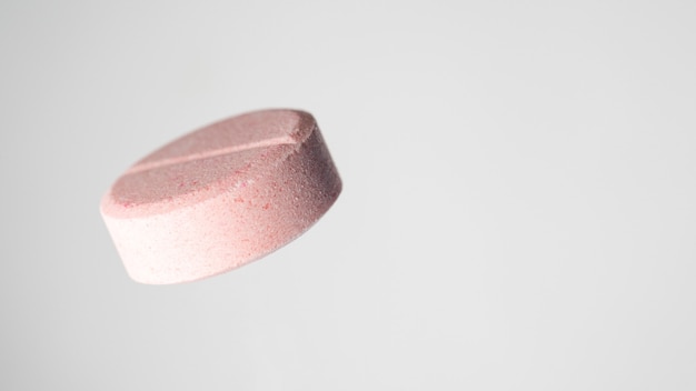 One pink medical ascorbic pill on light grey background. Isolated, close-up