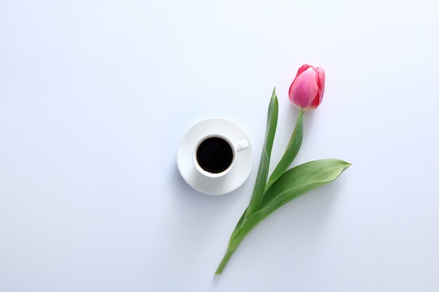 One pink tulip and coffee cup on white background Top view Flat lay