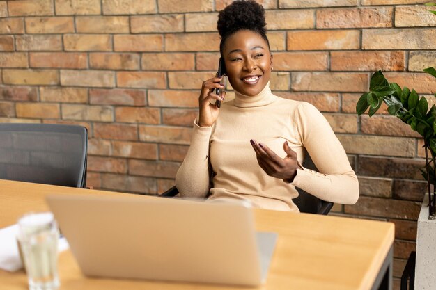 インダストリアルスタイルのオフィスのレンガの壁に座って携帯電話を使っている ⁇ 美しい若いアフリカ系アメリカ人のビジネスマン