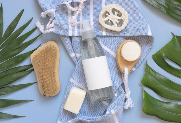 One pump dispenser on blue bath towel near tropical leaves and skin care accessories mockup