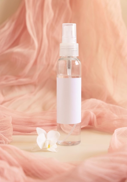 One pump dispenser bottle near white orchid flowers againts light pink tulle Mockup