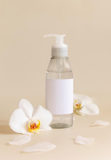 One pump dispenser bottle near white orchid flowers on light yellow close up Mockup