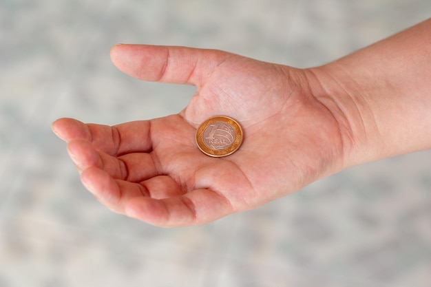 One real coin in the palm of a person's hand Hand holding a 1 dollar coin Real is the currency system of the Brazilian Government