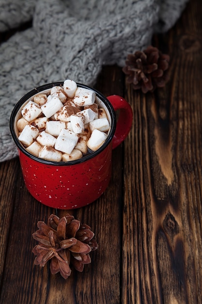 Foto una tazza rossa con bevanda calda con marshmallow e sciarpa lavorata a maglia sul natale in legno