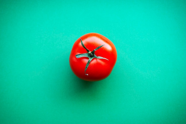 One red tomato on a green surface.