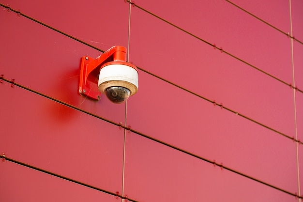 One red-white surveillance camera on red metal wall