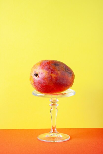 One ripe mango lies on a pedestal on a yellow background