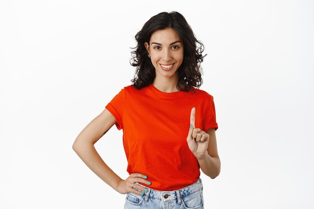 One rule. Smiling confident woman shows index finger and looking determined at camera, teaching lesson, explain something, standing over white background