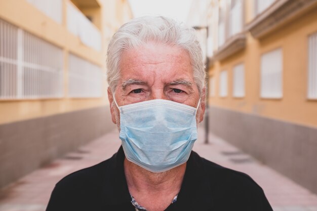 Una persona anziana o matura triste e sconvolta che guarda la telecamera indossando una maschera per prevenire il covid-19 o il coronavirus - stare a casa in quarantena e blocco - guardando la telecamera