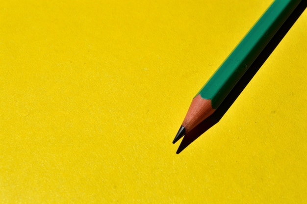 Photo one sharpened pencil lies on a yellow background. close-up.