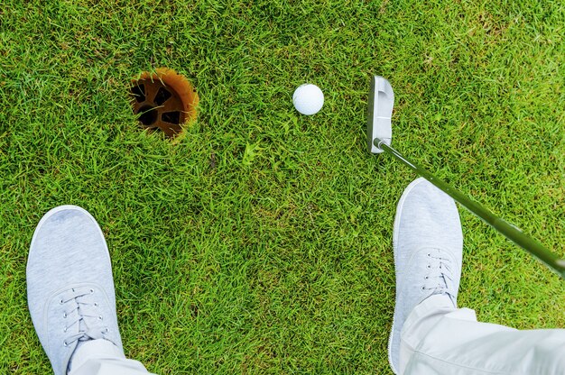 One shot to success. Top view of golfer putting while standing on green and near the hole