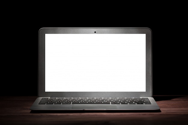 One silver modern laptop on wooden table in a dark room on black background.