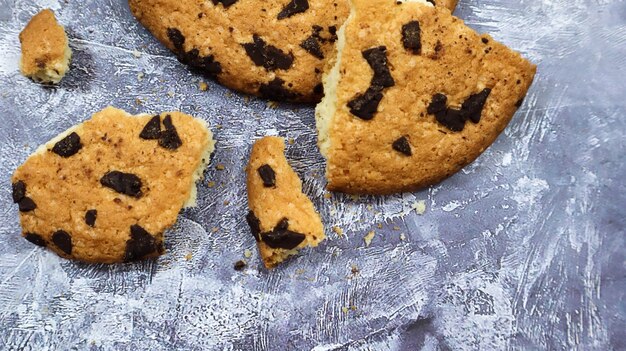 One soft freshly baked chocolate chip cookie with crumbs and chunks on a gray marble kitchen countertop. American traditional pastry, dessert. Delicious sweet food. Flat lay.