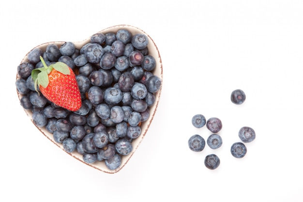 One strawberry and bluberries in  a heart shaped bowl