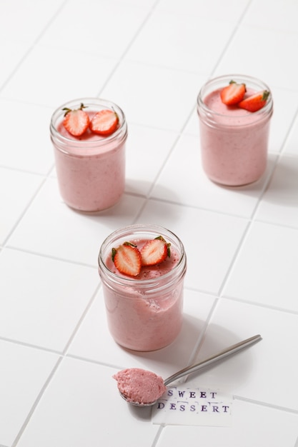 One strawberry dessert mousse in glass with spoon on white board on white tile background