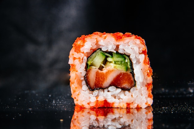 Photo one sushi roll on a black background is reflected from the mirror table