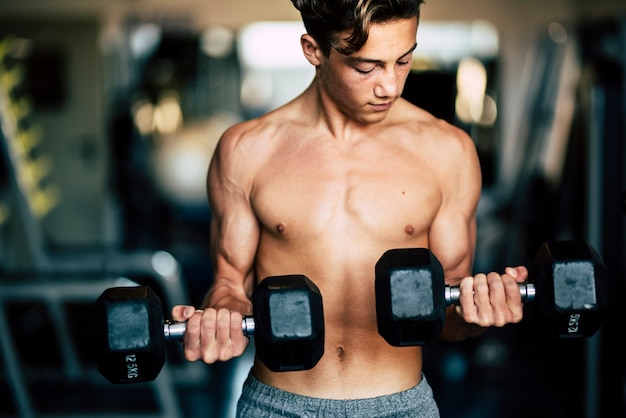 One teenager alone at the gym traning and lifting a dumbbels - strong and with muscles man - fitness and muscle lifestyle